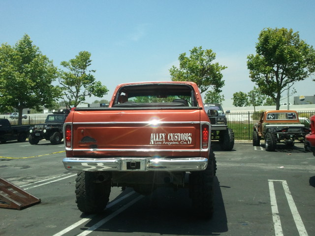 Orange pickup truck with 'Alley Customs Los Angeles, Ca.' on tailgate, parked next to other trucks