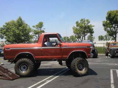 1978 Ford Bronco - An orange 1978 Ford Bronco is parked in a lot, showing its lifted suspension and large off-road tires.