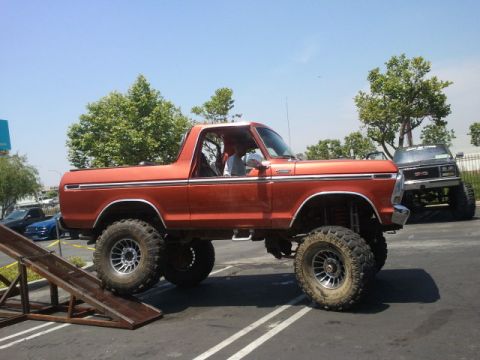 1978 Ford Bronco - Orange 1978 Ford Bronco on large tires, with a black GMC pickup truck in the background.