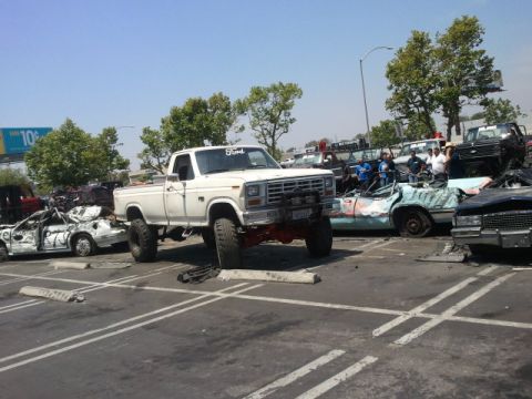 1978 Ford Bronco - White lifted pickup truck in a junkyard with multiple wrecked cars around it.