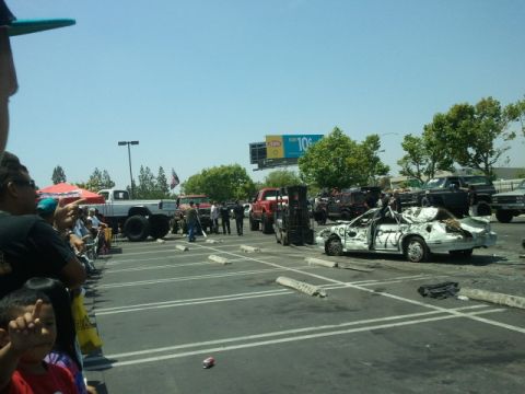 1978 Ford Bronco - A crowd watches as damaged vehicles are prepared for an event in a parking lot.