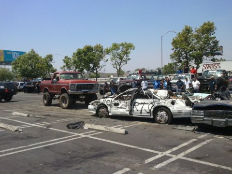 1978 Ford Bronco - A lifted red pickup truck is parked next to a heavily damaged white car with 'HELP 75' spray-painted on its side.