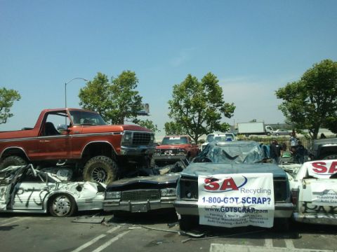 1978 Ford Bronco - Orange 1978 Ford Bronco sits atop a stack of crushed vehicles at a junkyard, with other cars and trucks in the background.