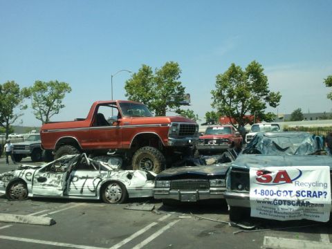1978 Ford Bronco - An orange 1978 Ford Bronco is parked on top of several crushed vehicles at a scrapyard.
