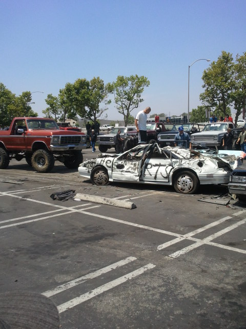 1978 Ford Bronco - A heavily damaged white sedan with graffiti is visible in a parking lot alongside other vehicles.