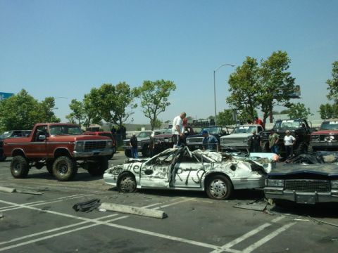 1978 Ford Bronco - A red lifted pickup truck is parked next to a heavily damaged white car with writing on it.