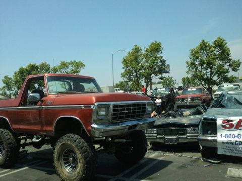 1978 Ford Bronco - Orange 1978 Ford Bronco with large tires and lifted suspension is parked in a lot with other vehicles.