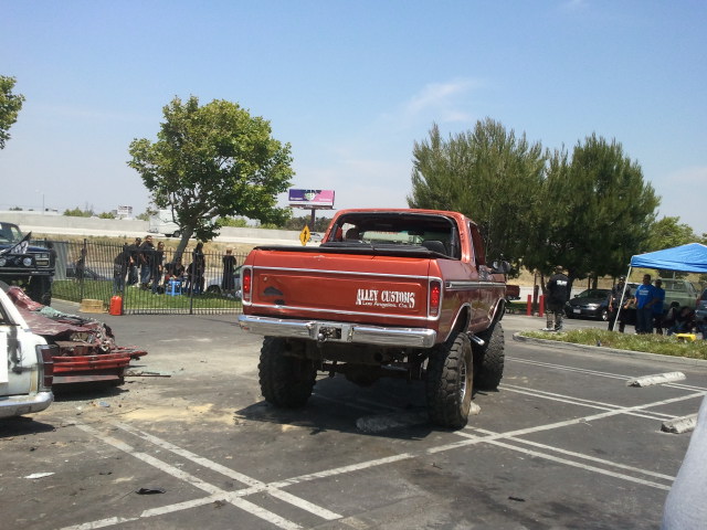 Orange pickup truck with custom paint and lifted suspension. Text on tailgate reads "ALLEY CUSTOMS"