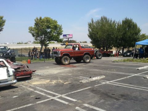 1978 Ford Bronco - A red 1978 Ford Bronco is driven in a parking lot, with other vehicles and spectators present.