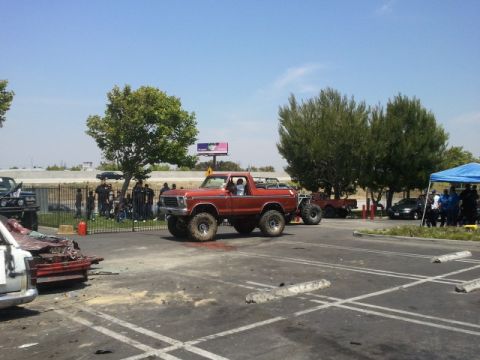 1978 Ford Bronco - A lifted red 1978 Ford Bronco is parked in a lot, with other vehicles and people visible in the background.