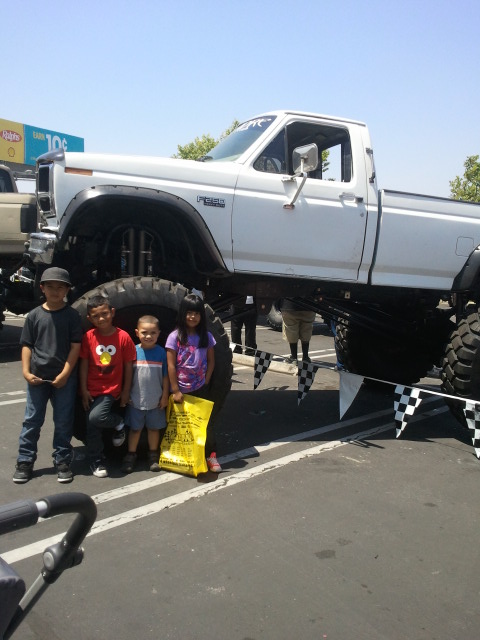 1978 Ford Bronco - A group of children pose in front of a heavily modified white pickup truck with oversized tires.