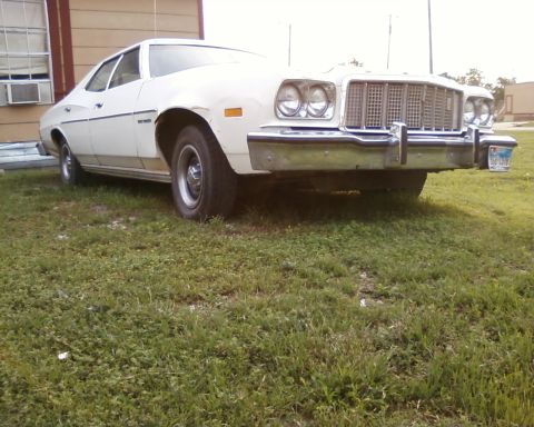 1976 Ford Torino - This white sedan is parked on a grassy area next to a building, showing its front grille and headlights.