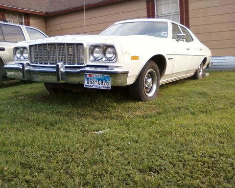 1976 Ford Torino - A white 1976 Ford Torino sedan is parked on a grassy area in front of a building.