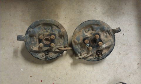 1991 Ford Festiva - These are two brake backing plates, likely for a drum brake system, resting on a concrete surface.