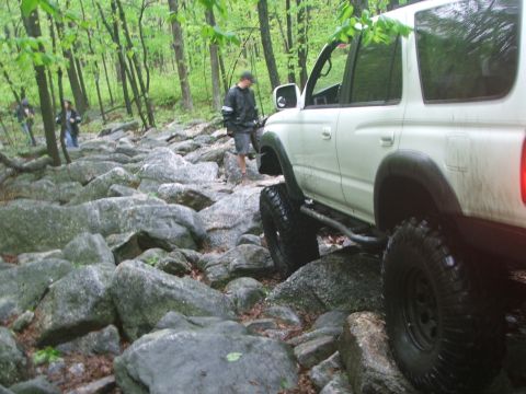 1996 Ford Bronco - A white SUV tackles a challenging rocky path in a wooded area.