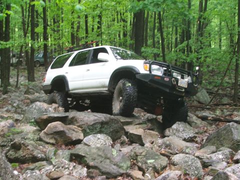 1996 Ford Bronco - Modified Toyota 4Runner tackling a challenging rocky trail in a wooded area.