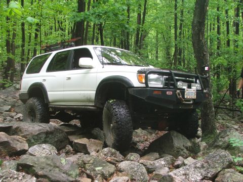 1996 Ford Bronco - A white Toyota 4Runner navigates a challenging rocky trail through a dense forest.