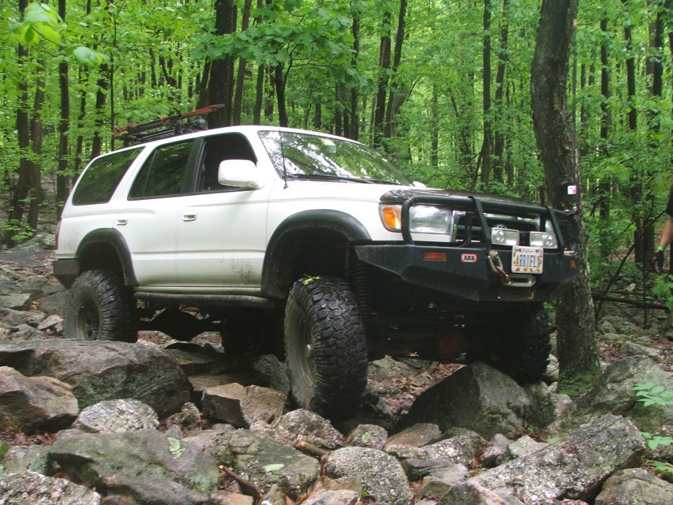 White Toyota 4Runner on rocky trail in woods. Has ARB bumper and roof rack