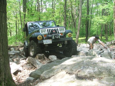 1996 Ford Bronco - A Jeep Wrangler tackles a challenging rocky trail with a person assisting.