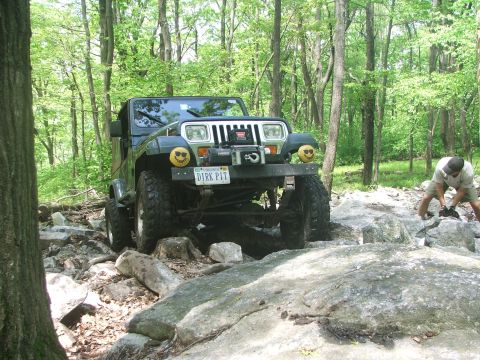 1996 Ford Bronco - A green Jeep Wrangler navigates a rocky trail with a winch and custom smiley face headlights.