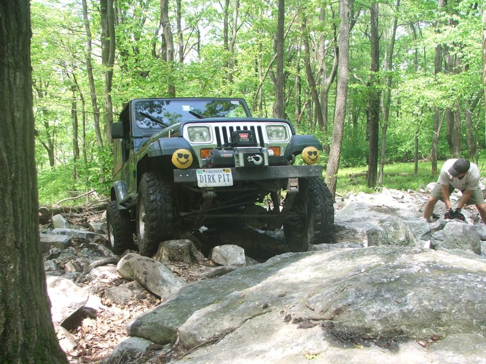 Green Jeep Wrangler on rocky terrain, front view. Winch on bumper, smiley face lights