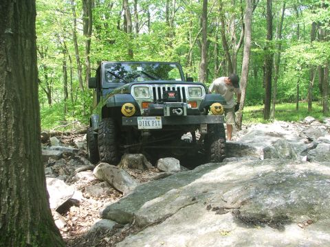 1996 Ford Bronco - A Jeep Wrangler TJ is shown off-road on a rocky trail, with a person standing nearby.