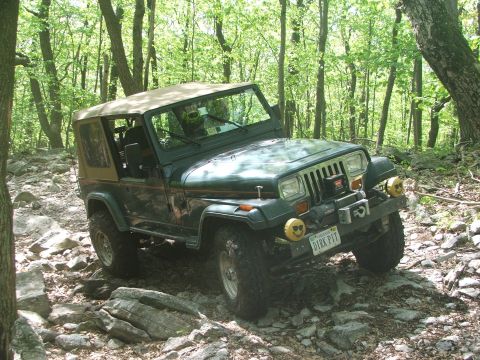 1996 Ford Bronco - Jeep Wrangler TJ navigating a challenging rocky off-road trail in a wooded area.