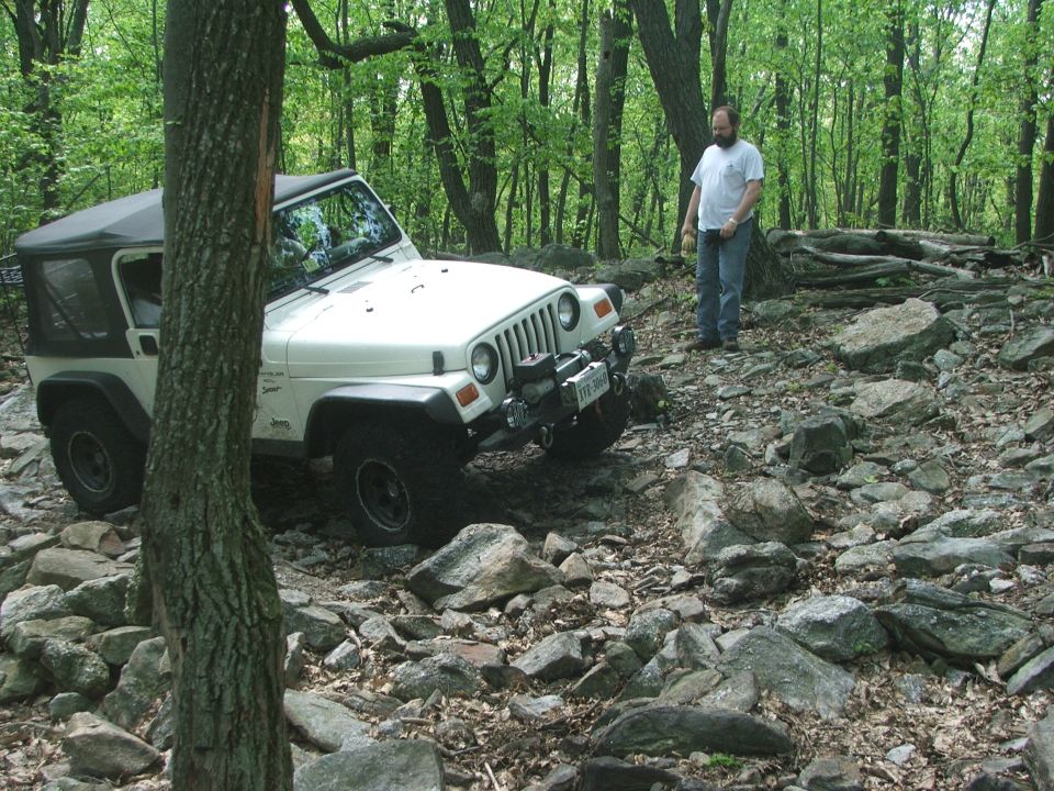 White Jeep Wrangler on rocky terrain with a man standing nearby