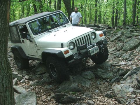 1996 Ford Bronco - A white Jeep Wrangler TJ tackles a challenging rocky path surrounded by trees.
