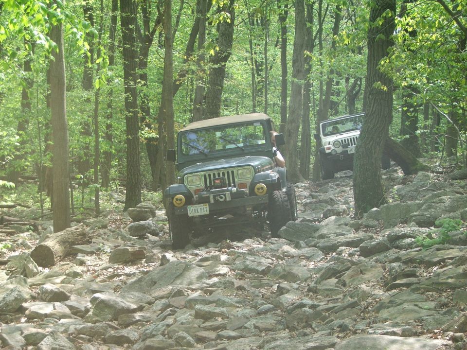 Dark green Jeep Wrangler on rocky terrain, front view. License plate reads "VIRS PIT"