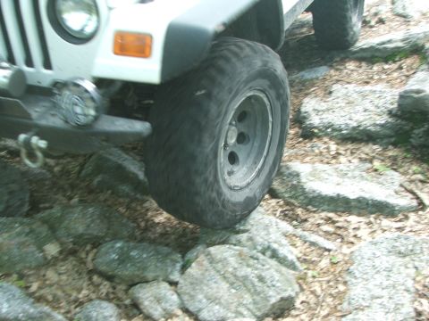 1996 Ford Bronco - A Jeep Wrangler navigates a rocky trail, its tire angled over a large stone.