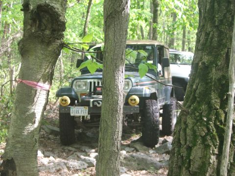 1996 Ford Bronco - Two off-road vehicles are parked on a rocky trail surrounded by trees.