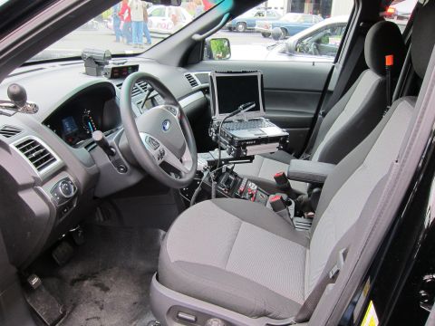 1991 Ford LTD Crown Victoria - Front cabin of a black police SUV showing cloth seats, a Ford steering wheel and a center-mounted laptop computer.