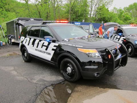 1991 Ford LTD Crown Victoria - black-and-white Ford Police Interceptor SUV lettered TO PROTECT AND TO SERVE parked beside other cruisers in a paved lot.