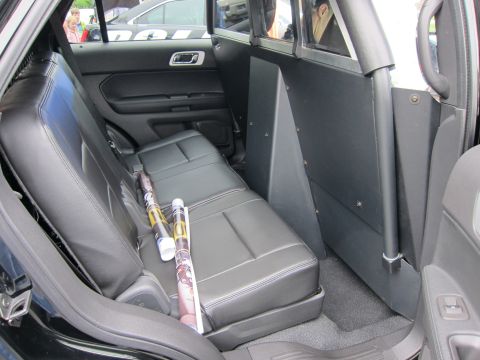 1991 Ford LTD Crown Victoria - black vinyl rear bench seat of a police SUV behind a partition, with rolled poster tubes resting on the cushion.