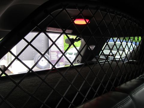 1991 Ford LTD Crown Victoria - Interior view looking through a black diamond-mesh prisoner partition toward the rear windows of a police vehicle.