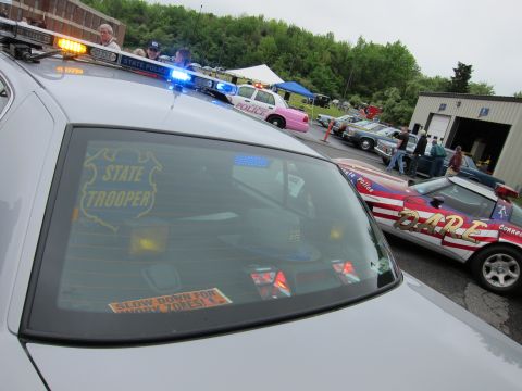 1991 Ford LTD Crown Victoria - Rear window of a silver state trooper car with STATE TROOPER decal, parked in a lot among cruisers and a patriotic D.A.R.E. car.