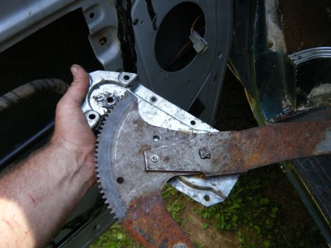 1981 Ford E350 - Rusty window regulator mechanism being held by a hand, removed from a vehicle door.