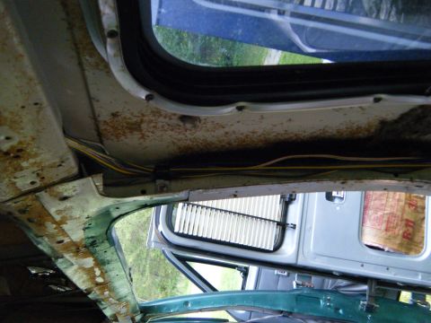 1981 Ford E350 - The interior of an older vehicle shows significant rust and exposed wiring, with a glimpse of another vehicle's door visible through the wi…