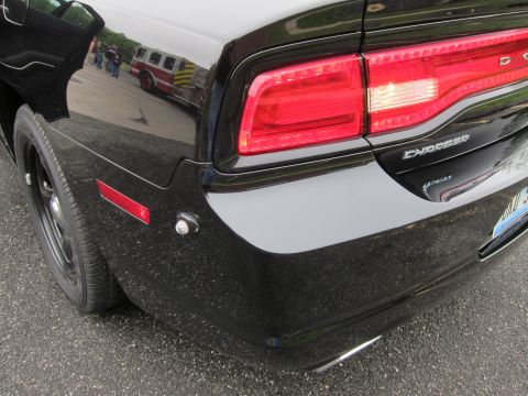 1991 Ford LTD Crown Victoria - Close-up of a black Dodge Charger's rear quarter with its taillight, Charger badge and a red reflector, a fire truck reflected in the paint.