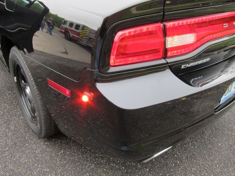 1991 Ford LTD Crown Victoria - rear quarter of a black Dodge Charger glints with a glowing red side-marker light, taillight and Charger badge visible.