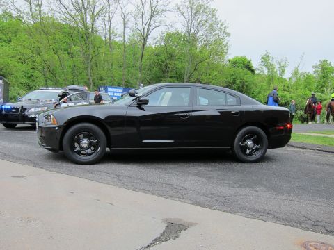 1991 Ford LTD Crown Victoria - Side profile of a black Dodge Charger sedan parked at a curb, with people and another cruiser in the background.