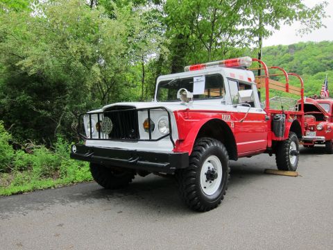 1991 Ford LTD Crown Victoria - vintage red-and-white 4x4 fire brush truck with brush guard, roof light and stake bed parked on a tree-lined road.