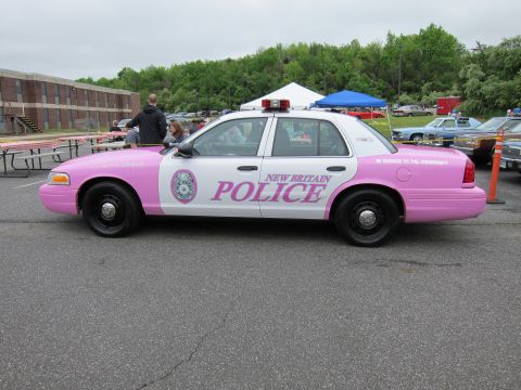 1991 Ford LTD Crown Victoria - Side profile of a pink-and-white Ford Crown Victoria marked New Britain Police with a department seal and roof light bar.