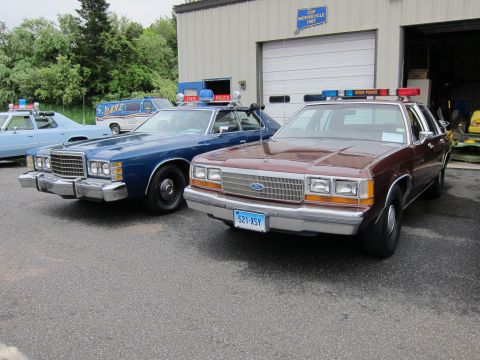 1991 Ford LTD Crown Victoria - maroon Ford LTD Crown Victoria State Police cruiser parked beside an older blue police sedan near a garage.