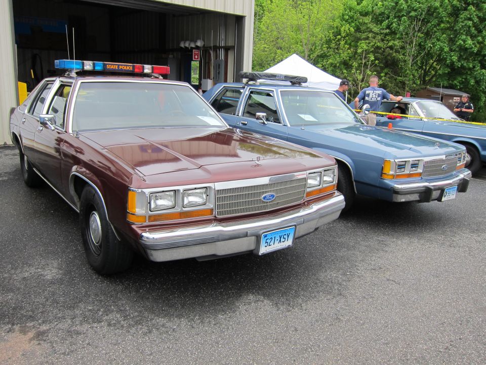 Maroon and blue Ford State Police sedans parked side by side near garage