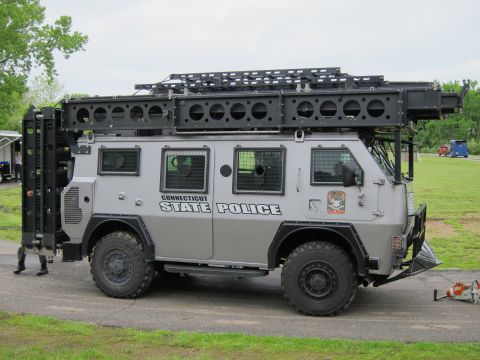 1991 Ford LTD Crown Victoria - gray Connecticut State Police armored tactical truck with a tall roof rack parked on pavement near a field.