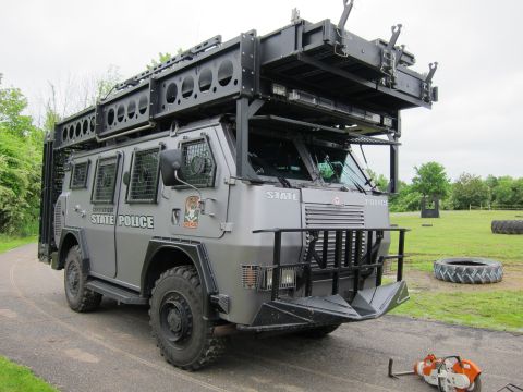 1991 Ford LTD Crown Victoria - gray Connecticut State Police armored 4x4 tactical truck shown from the front quarter on a paved path by a field.