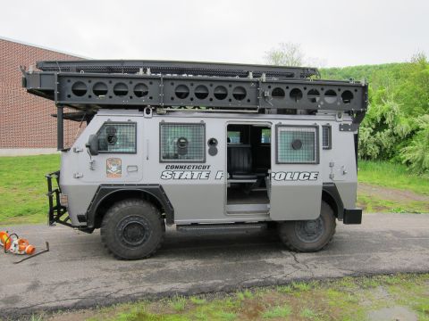 1991 Ford LTD Crown Victoria - gray Connecticut State Police armored 4x4 tactical truck with its side door open, parked near a brick building.