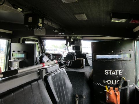 1991 Ford LTD Crown Victoria - Interior rear view of an armored tactical police vehicle showing bench seating, a gun mount, and a riot shield labeled STATE POLICE.